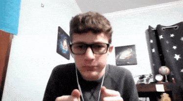 a young man wearing glasses and headphones looks at the camera in a bedroom