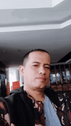 a man wearing a camouflage jacket and a blue shirt takes a selfie