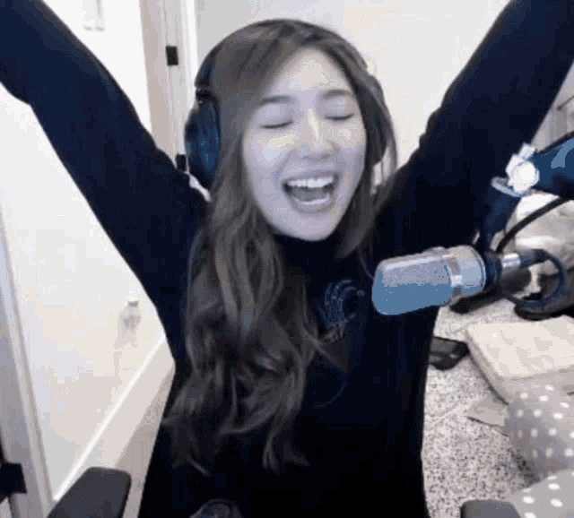 a woman wearing headphones is sitting in front of a microphone with her arms outstretched .