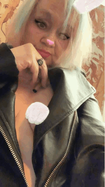 a woman wearing a black leather jacket has a pink nose and a ring on her finger