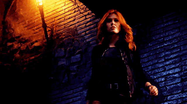 a woman in a black jacket is standing in front of a brick wall .