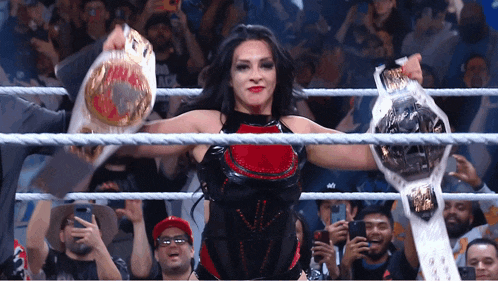 a woman in a wrestling ring holds up two belts in front of a crowd