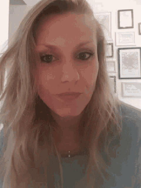 a close up of a woman 's face with a wall of framed pictures behind her