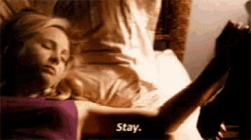 a woman is laying in bed with her eyes closed and a man is holding her arm and says stay .