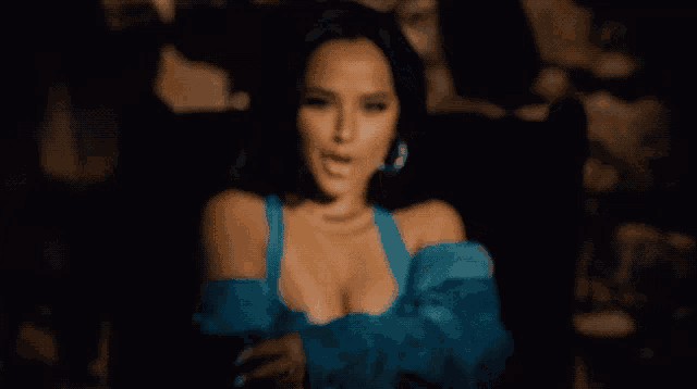 a woman in a blue off the shoulder top is sitting in a dark room