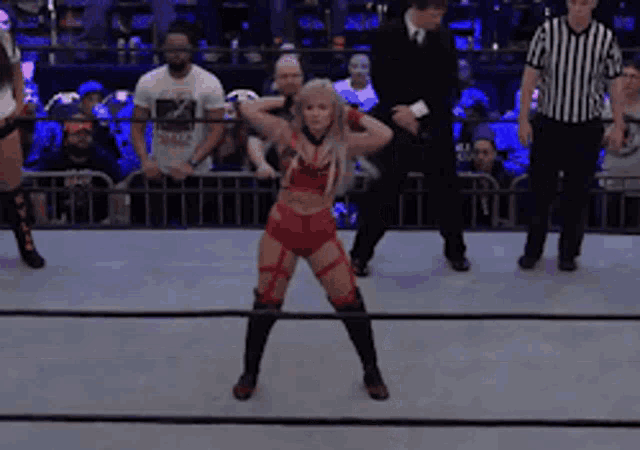 a woman in a red outfit is standing in a wrestling ring with a referee standing behind her