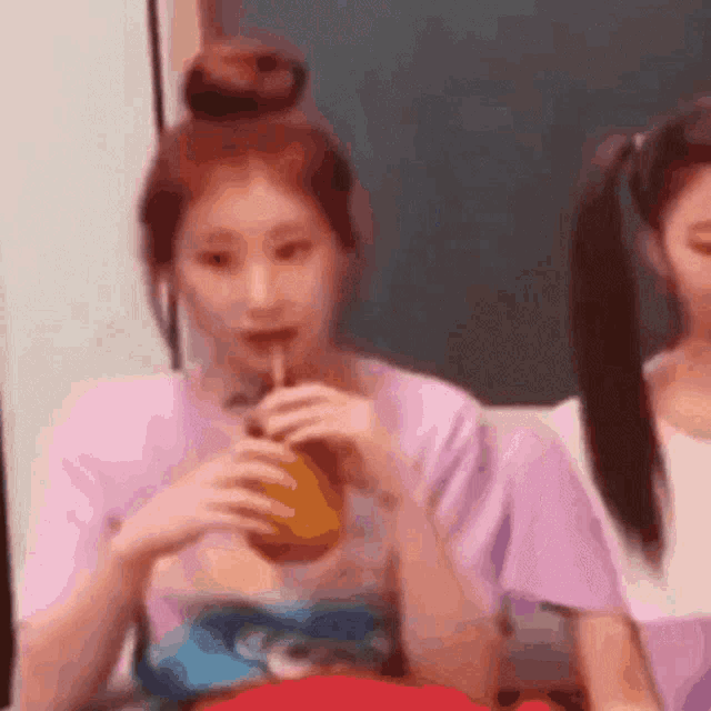 a girl is drinking a drink through a straw while another girl looks on .