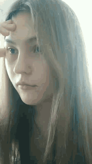 a young girl with long hair is touching her forehead with her hand .