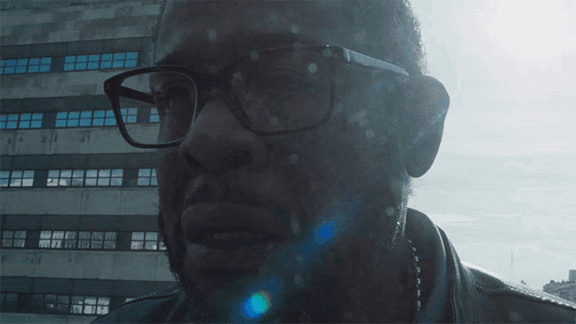 a man wearing glasses and a leather jacket looks at the camera