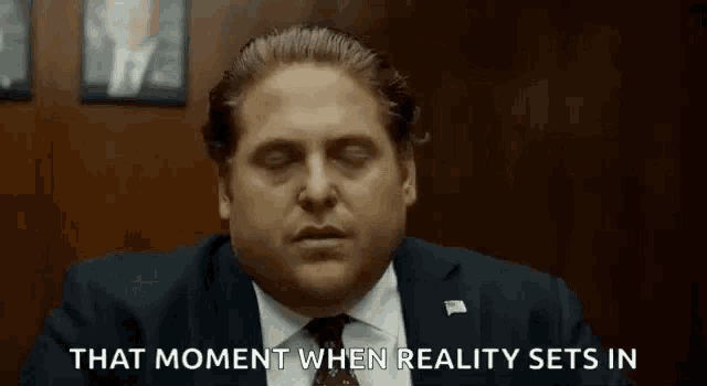 a man in a suit and tie is sitting in a room with his eyes closed and says that moment when reality sets in