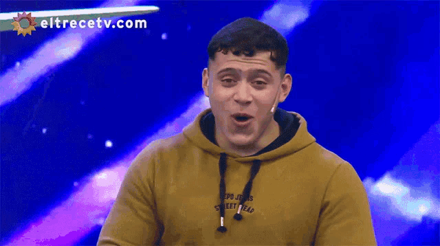 a man in a yellow hoodie is laughing with eltrecetv.com behind him