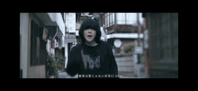 a man wearing a black shirt with a butterfly on it is standing on a street .