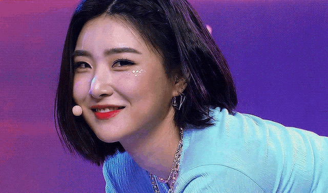 a close up of a woman 's face wearing a blue shirt and earrings