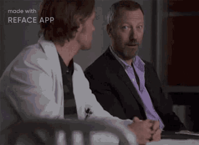 two men are sitting at a table talking to each other . one of the men is wearing a purple tie .