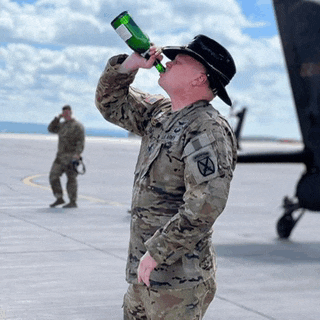 a man in a military uniform drinks from a green bottle