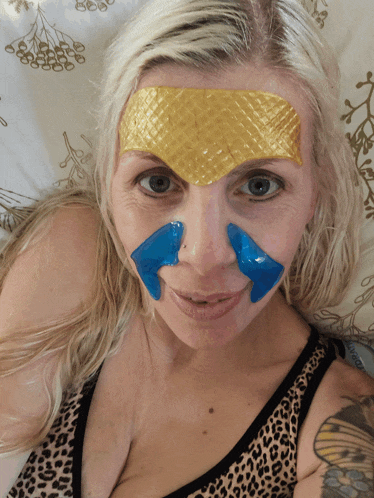 a woman laying on a bed with a gold and blue patch on her forehead