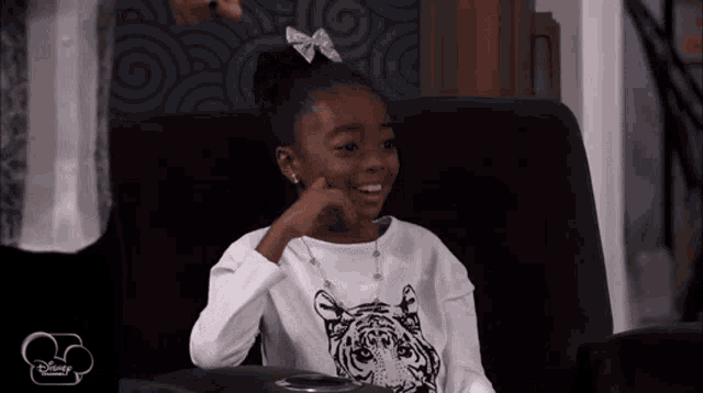 a little girl wearing a tiger shirt is sitting in a chair