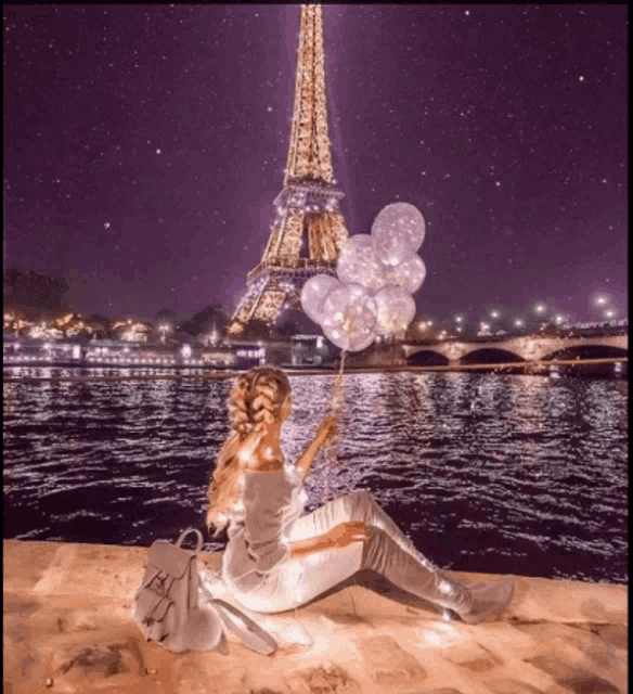 a woman holding balloons in front of the eiffel tower at night