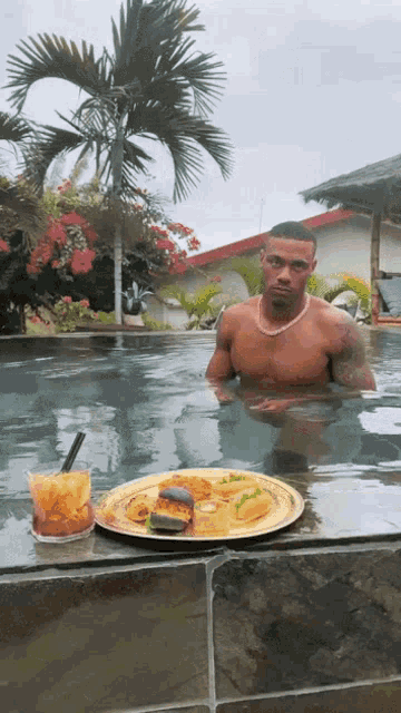 a man in a swimming pool with a plate of food and a drink on the edge