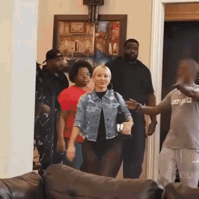 a woman in a denim jacket is standing in a living room with a group of men .