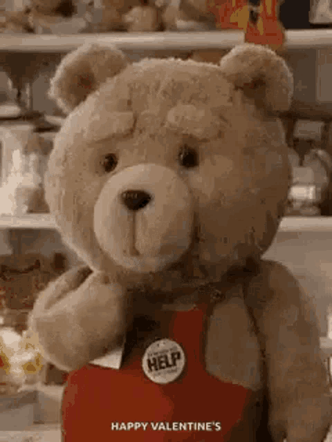 a teddy bear is holding a heart shaped box and wearing a help badge .