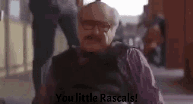 a man with glasses and a mustache is sitting in a chair and saying `` you little rascals! ''