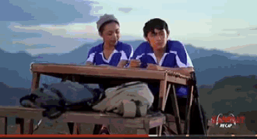 a boy and a girl are sitting at a table in front of mountains .