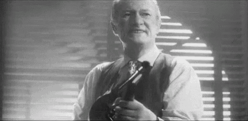 a man in a suit and tie is holding a gun in his hand in a black and white photo .