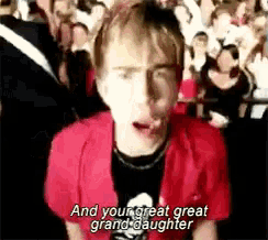 a man in a red shirt is standing in front of a crowd and singing .