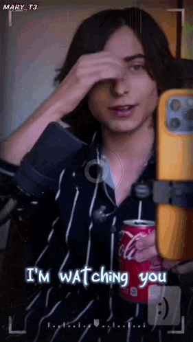 a man is holding a can of coca cola while taking a picture of himself .