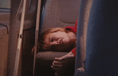 a woman in a red shirt is laying in a car with her mouth open