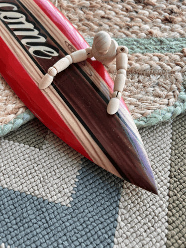 a wooden mannequin sits on a surfboard that says come
