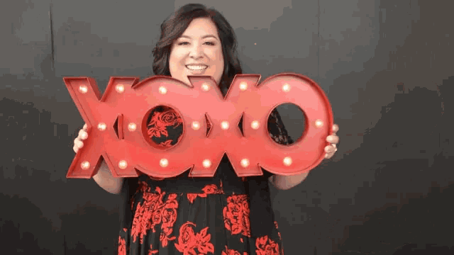 a woman in a red dress is holding a large red sign that says xoxo