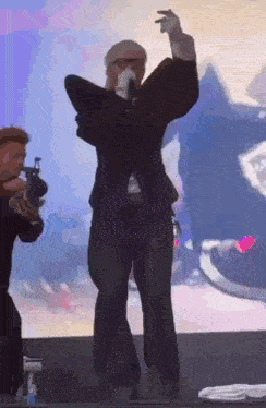 a man in a suit is singing into a microphone on a stage while another man holds a gun .