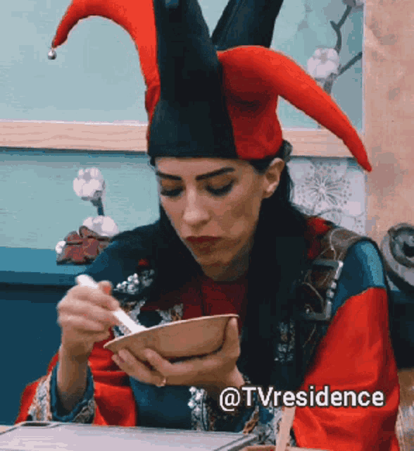 a woman wearing a jester hat is eating from a bowl with a spoon