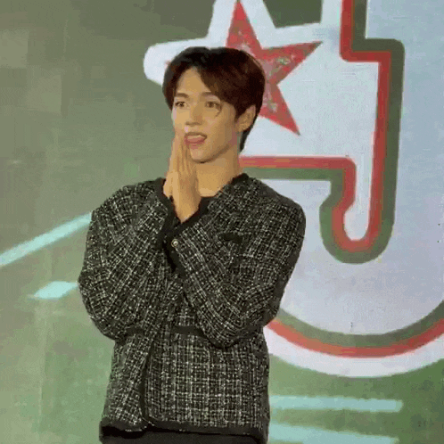 a young man in a black and white jacket is standing in front of a wall with a red star on it .