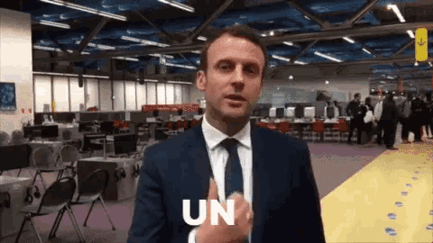 a man in a suit and tie is giving a thumbs up and says " un "