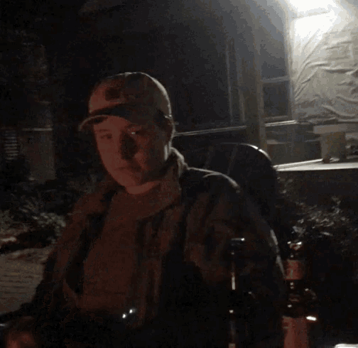 a man in a baseball cap is sitting in front of a fire at night