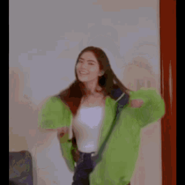 a woman is standing in front of a mirror wearing a green jacket and black jeans .