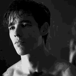 a black and white photo of a shirtless young man looking at himself in a mirror .