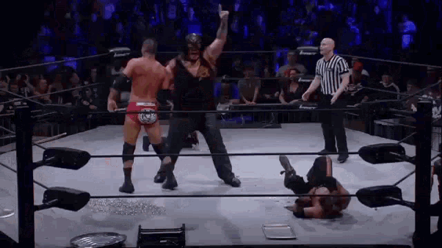 two men are wrestling in a ring with a referee in the background .