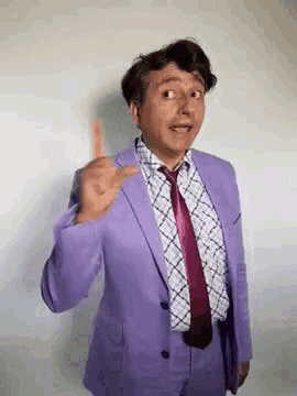 a man in a purple suit and tie is giving the middle finger .
