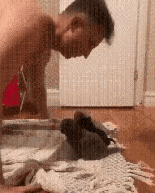 a man without a shirt is playing with a kitten on a rug .