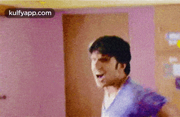a man in a blue shirt is standing in front of a door and making a funny face .