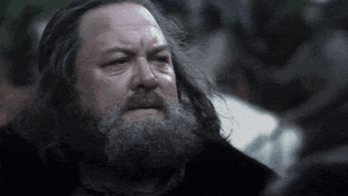 a man with long hair and a beard is looking down