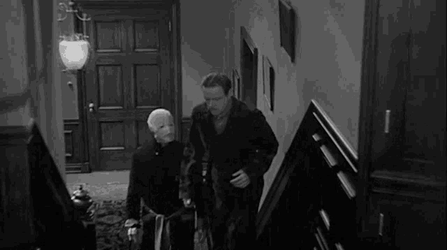 two men are standing next to each other in a room in a black and white photo .