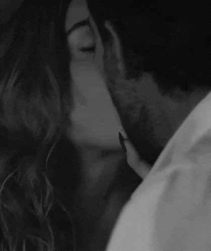a black and white photo of a man and a woman kissing .