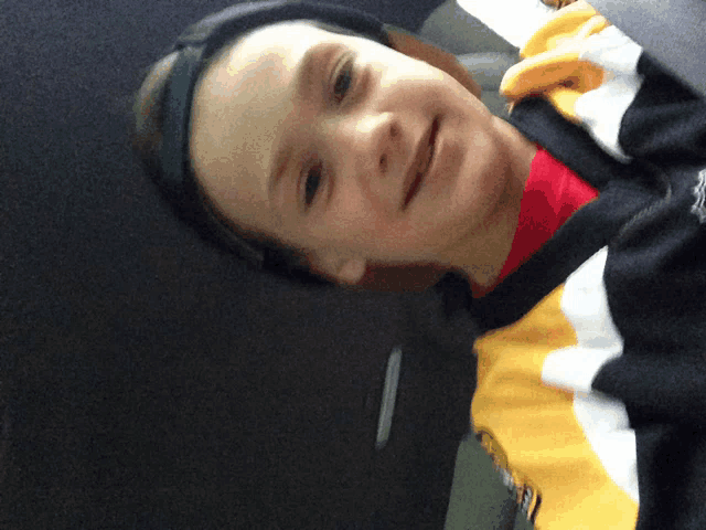 a young boy wearing a black hat and a yellow and white sweater smiles for the camera