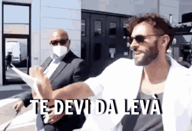 a man wearing sunglasses and a white jacket says " te devi da leva "