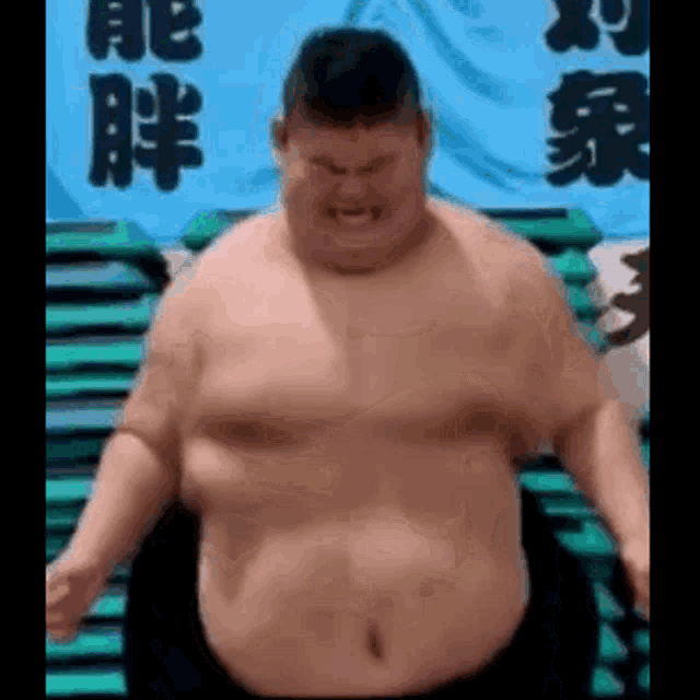 a very fat man without a shirt is standing in front of a stack of green chairs .